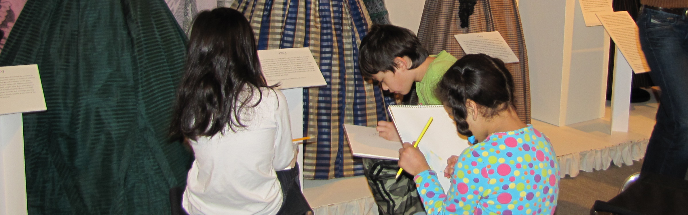 Image of children looking at an exhibit and working on an activity on sheets of paper.