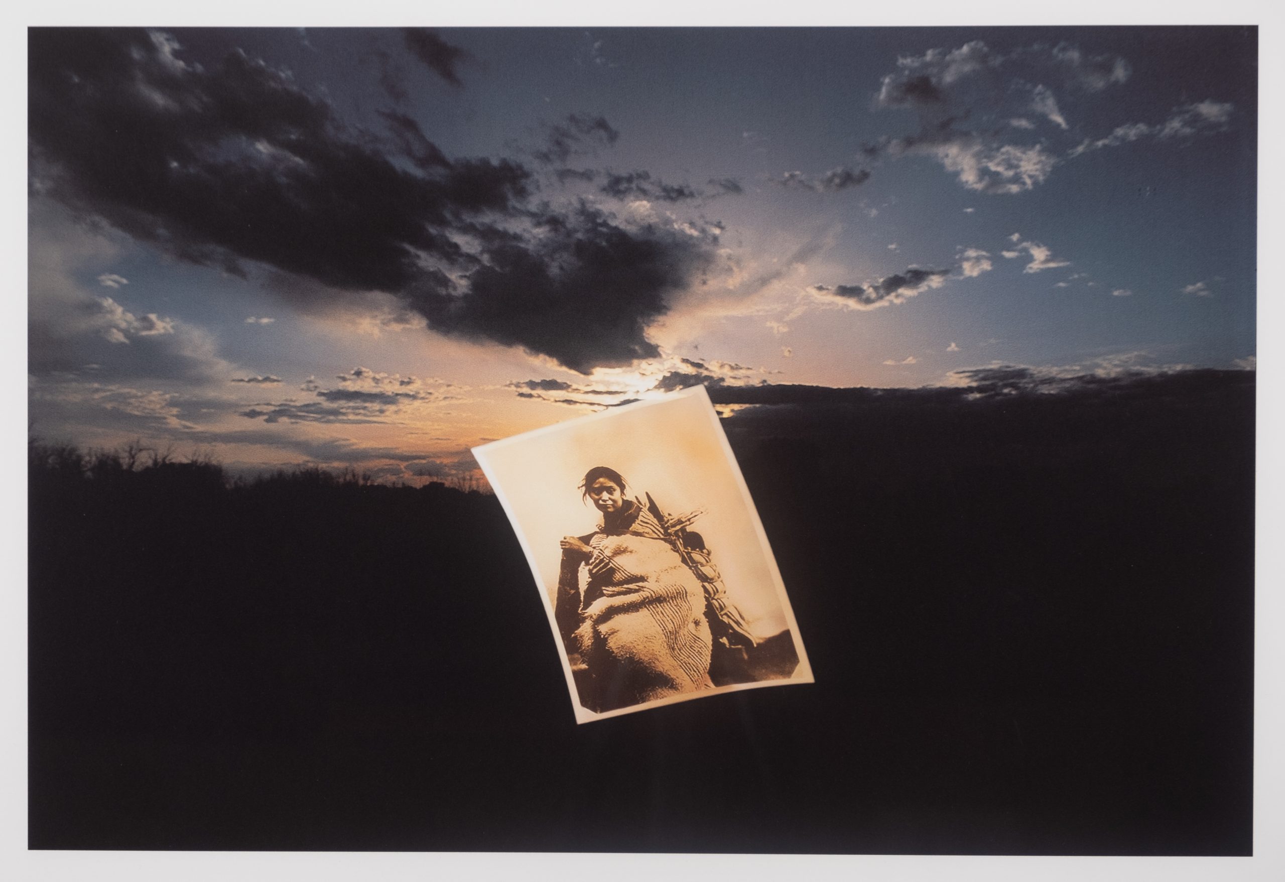 1998.1.3: Photograph of woman on landscape with cloudy sky.